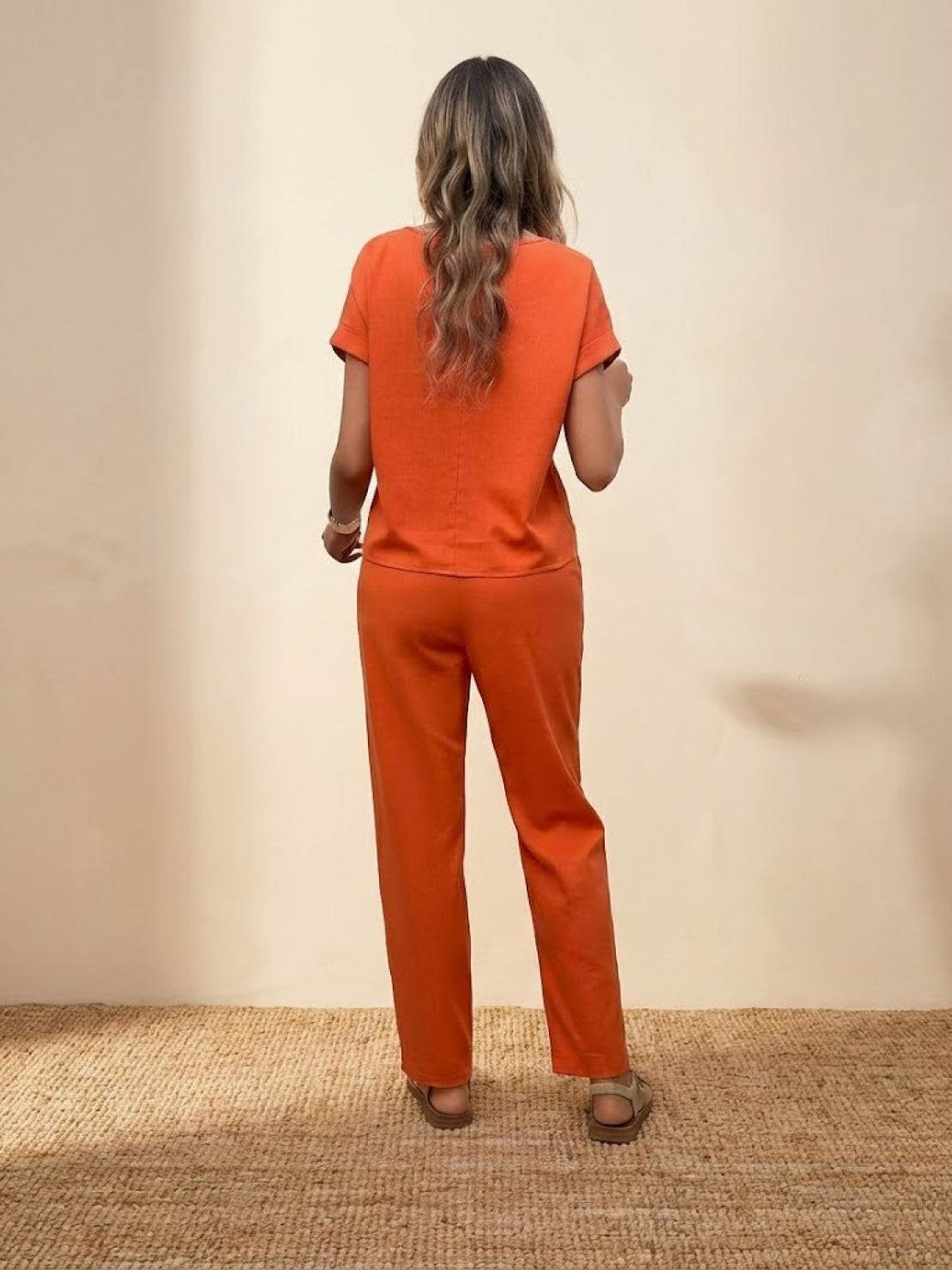woman wearing orange 100 cotton total comfort two-piece set from the back standing on woven mat against beige background