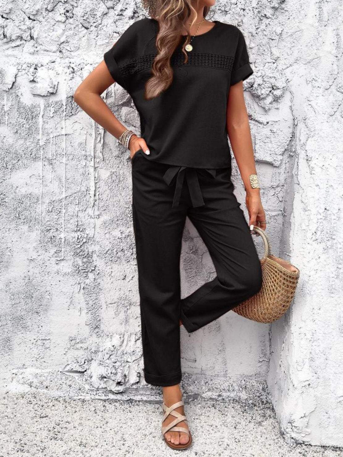 Woman wearing black 100% cotton total comfort two-piece travel set with short sleeves and drawstring pants against white textured wall.