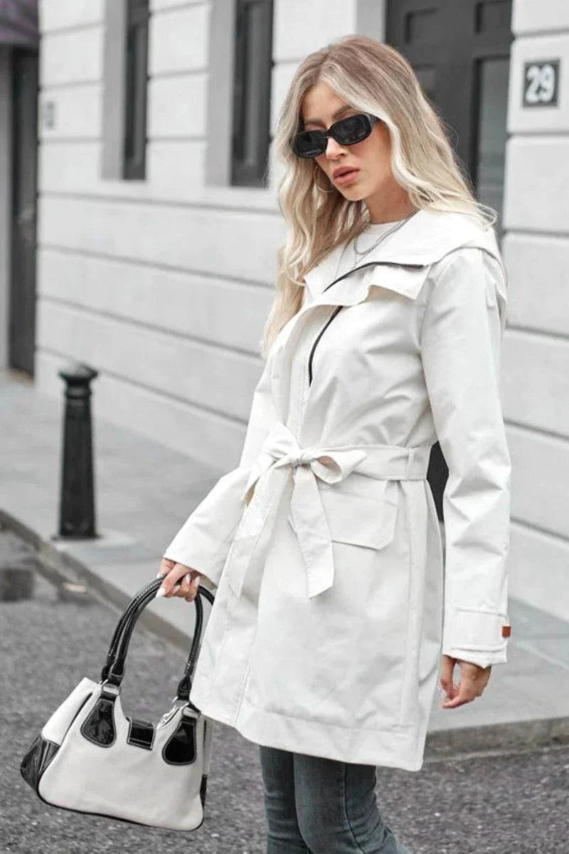 Woman wearing white water-resistant windbreaker trench jacket with belt and sunglasses outdoors