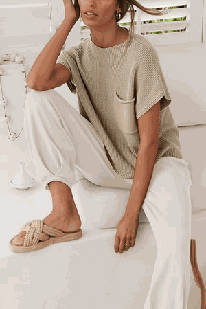 Woman wearing Comfy Couture Knit Sweater two-piece set with beige knit pullover and white high-waisted pants sitting indoors