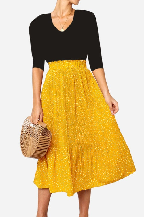 Woman wearing an effortlessly chic yellow polka dot pleated midi skirt with a high waist and black top carrying a wooden handbag.