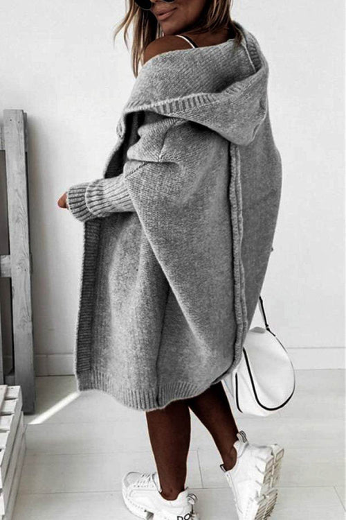 Woman wearing warm oversized hooded grey cardigan with white sneakers and handbag indoors