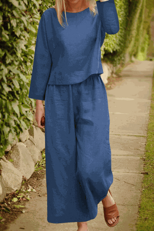 Woman wearing a loose solid color two-piece set with long sleeves and wide-leg pants in blue walking outdoors