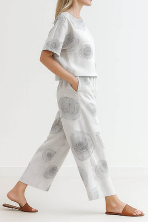 Woman wearing a light grey loose fit co-ord set with wide-leg pants and short-sleeve top featuring subtle circular patterns, paired with brown sandals.