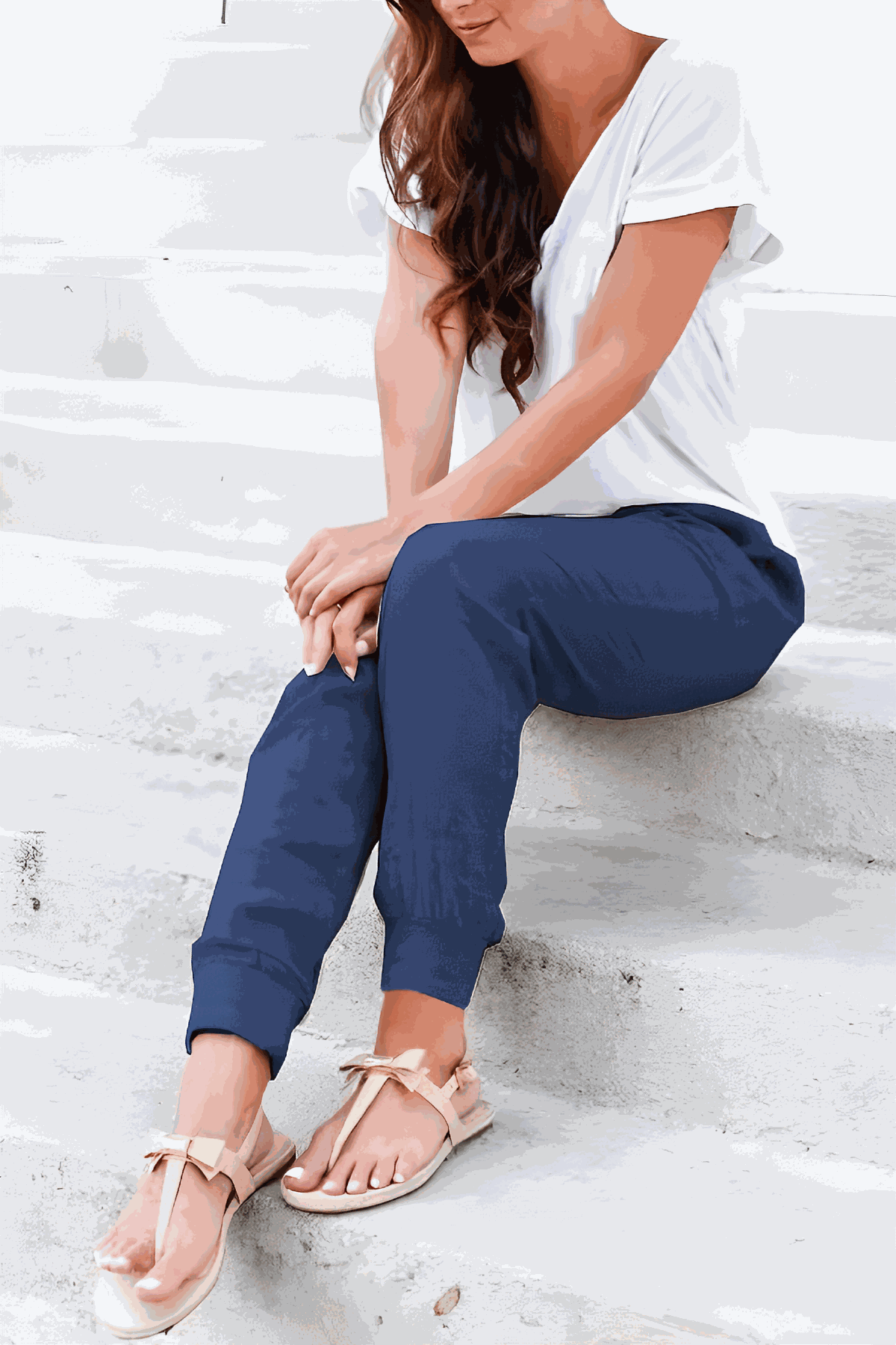 Woman wearing relaxed chic elastic ankles pants in navy blue sitting on stairs with white top and sandals