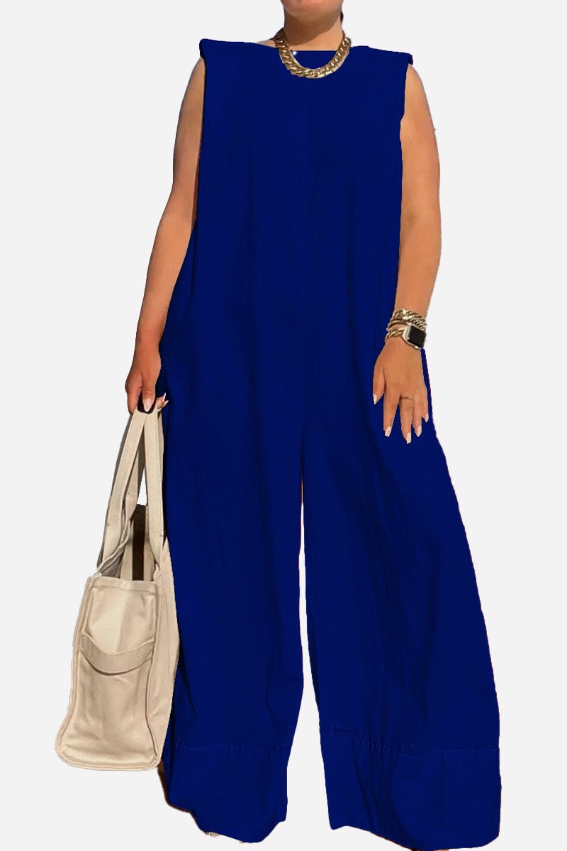 Blue sleeveless wide-leg jumpsuit with shoulder pads, accessorized with gold jewelry and a beige handbag.