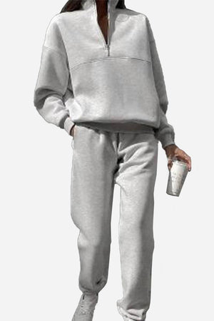 Woman wearing gray cotton-blended two-piece tracksuit with high collar and zipper, holding a cup.