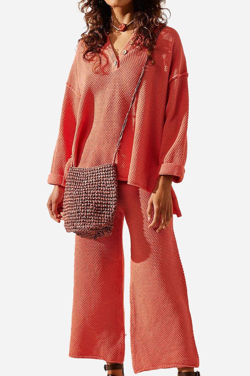 Woman wearing coral pink textured oversized two-piece set with wide pants and long sleeves, styled with a woven crossbody bag, showcasing multi-weather comfort clothing.