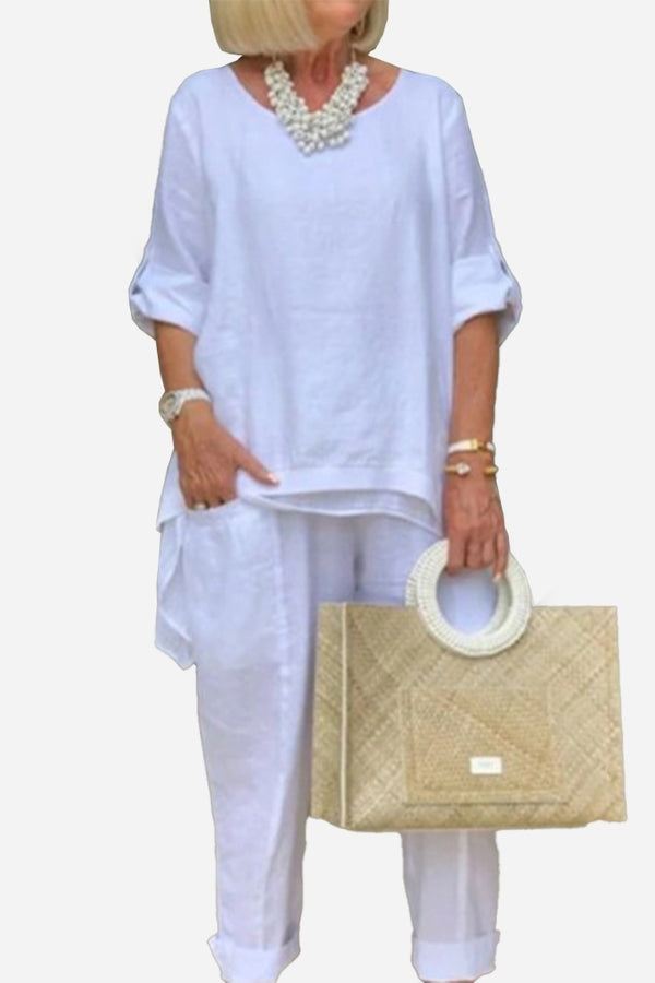 Woman wearing white asymmetrical two-piece trouser set with rolled sleeves and holding woven handbag