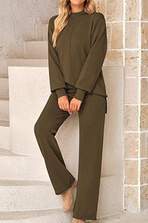 Woman wearing olive green high neck sweater and wide leg pants set standing against beige wall