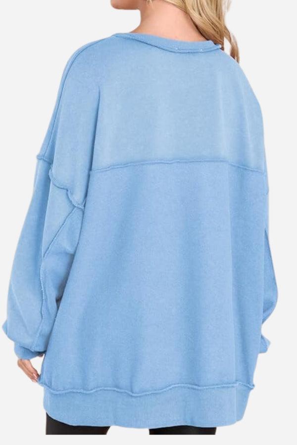 Back view of a light blue oversized urban sweatshirt with a slouchy fit and raw seam details worn by a person with blonde hair.