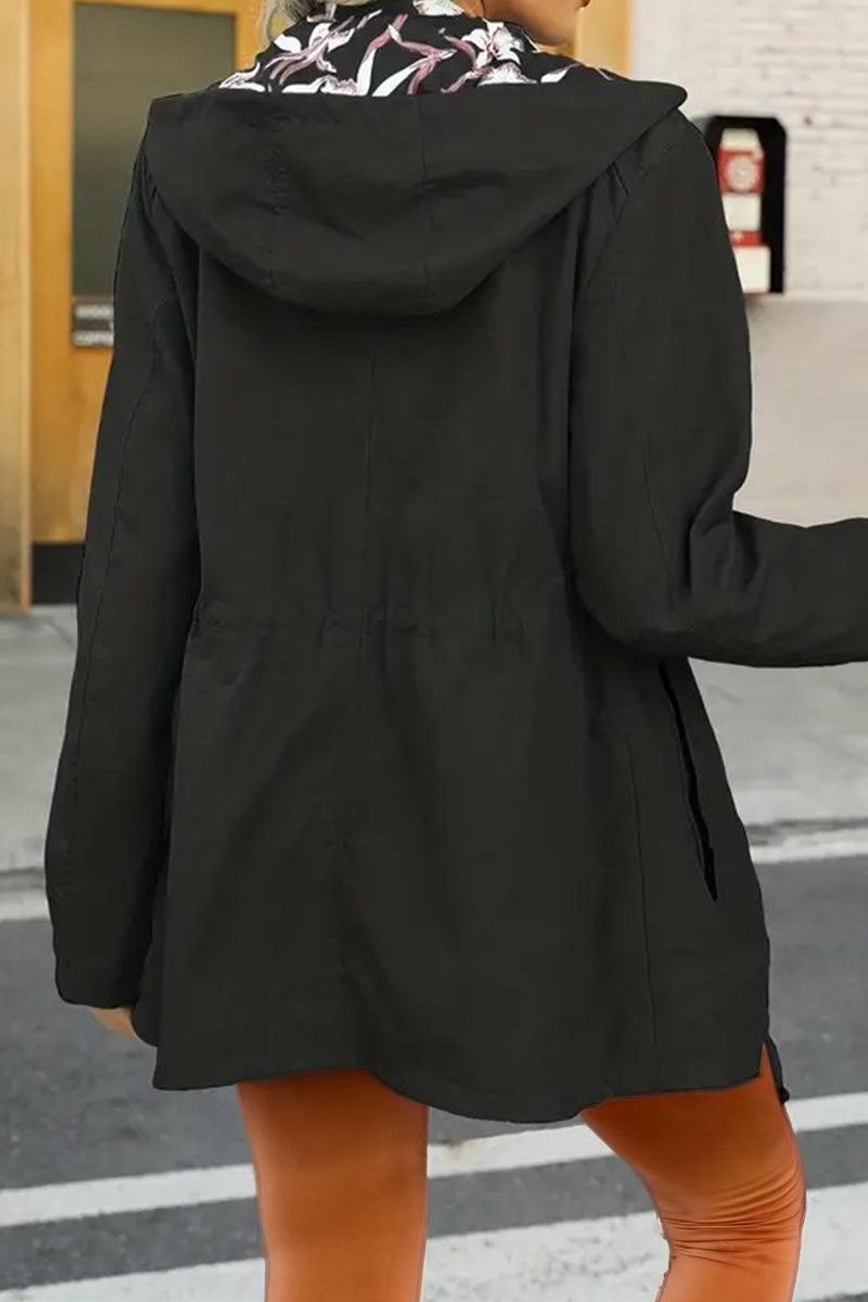 Back view of a black reversible floral raincoat with a hood worn by a person outdoors