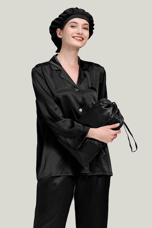 Black Mulberry Silk Pajama Set with matching sleep cap shown on model holding a silk pouch
