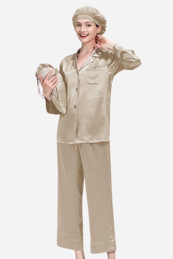 Woman wearing classic beige Mulberry silk pajama set with matching sleep cap, holding another cap in hand