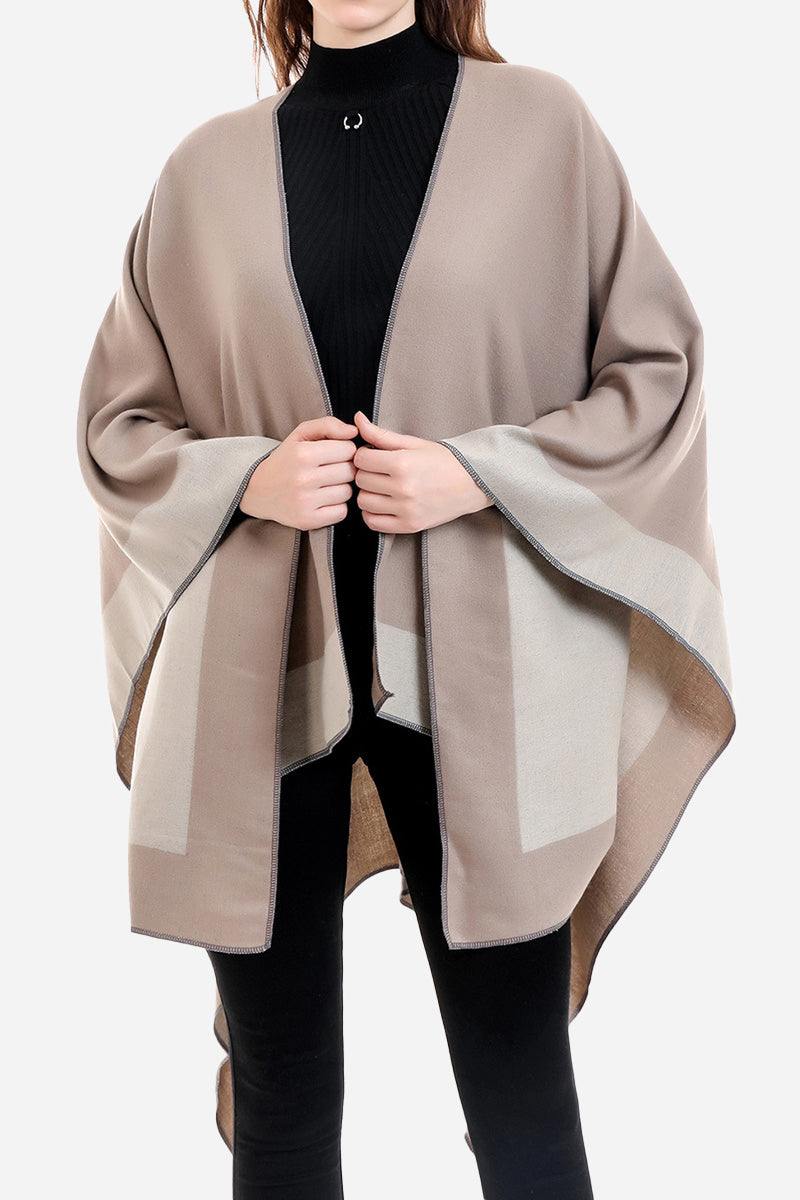 One size elegant knitted poncho in two-tone beige and taupe colors with flowing silhouette worn over black outfit