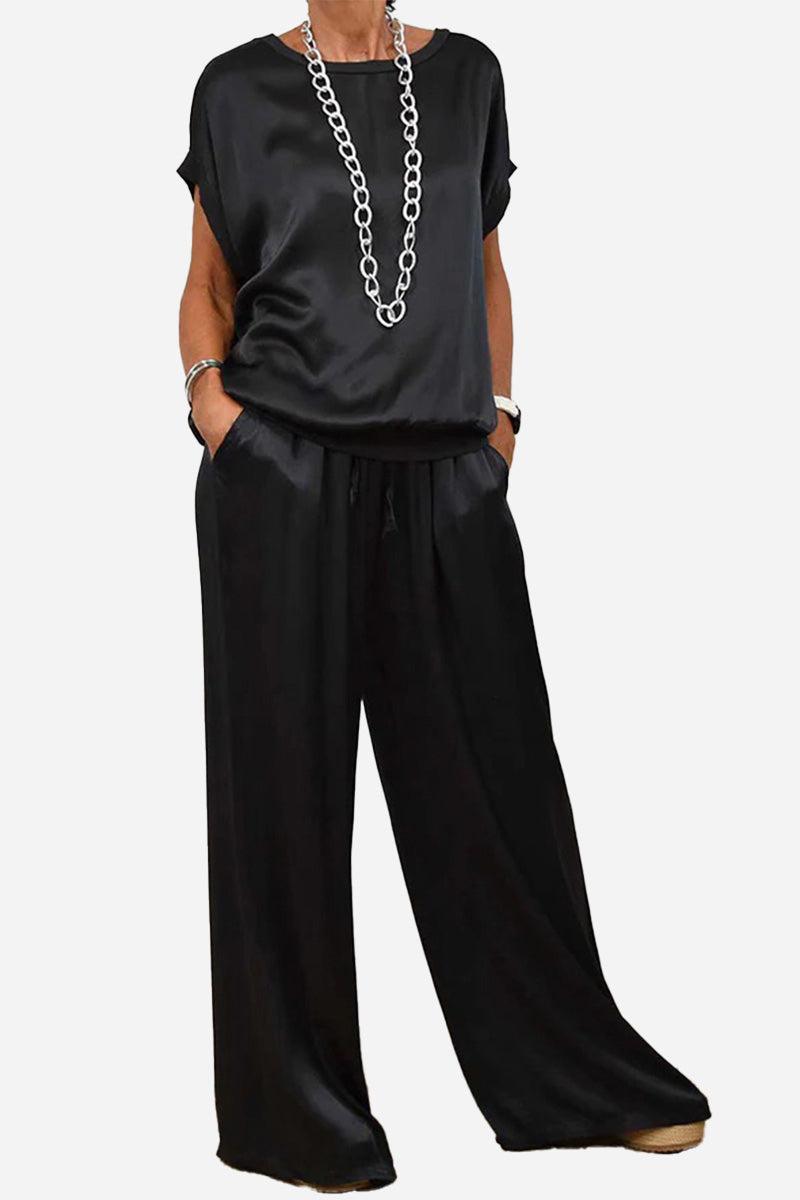 Black satin Silken Escape two-piece set with wide-leg pants and short-sleeve top with pockets and silver chain necklace
