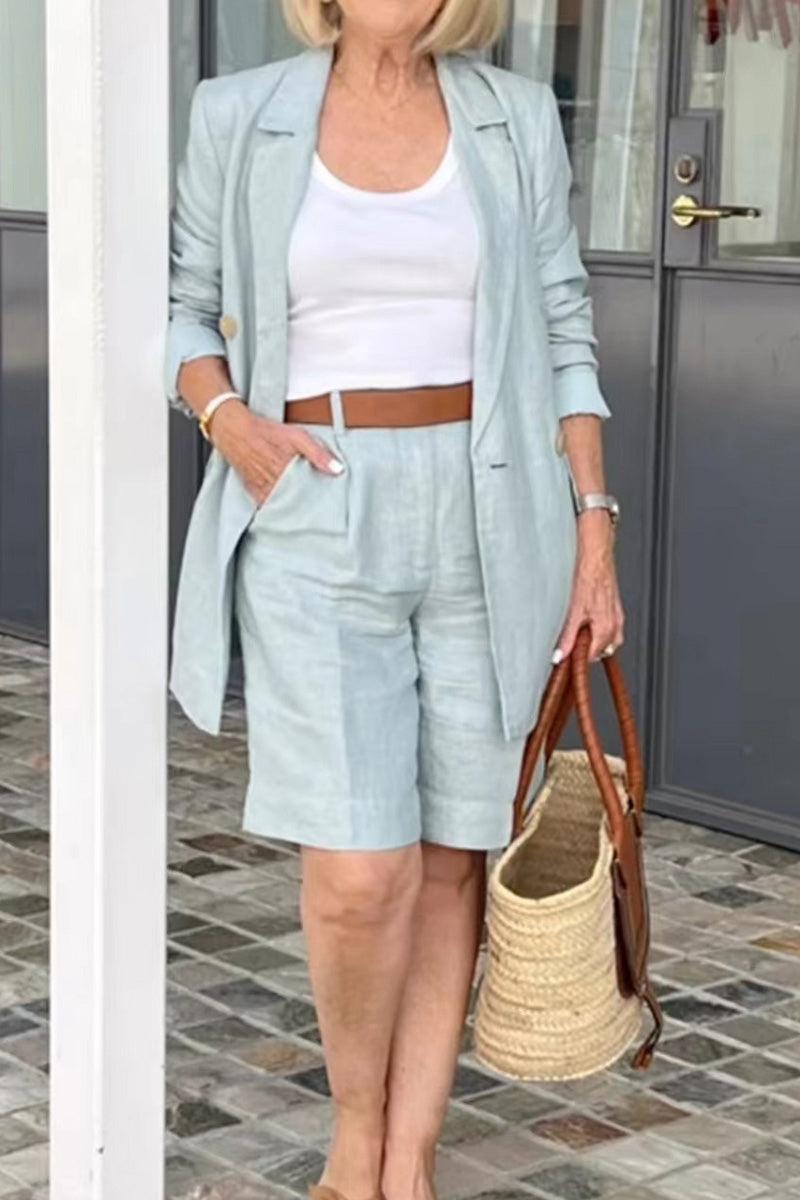 Stylish blazer and shorts two-piece set in light pastel, worn with white tank top and brown belt, paired with woven handbag.