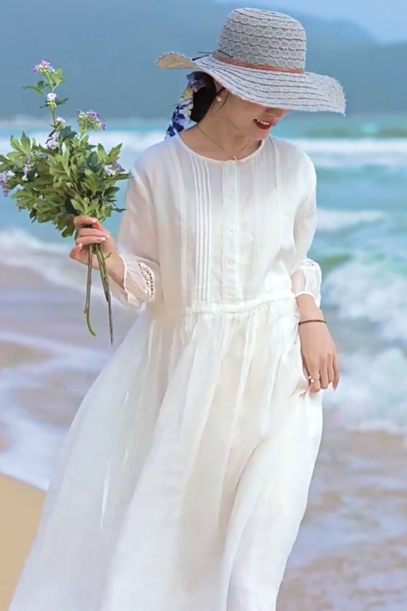 woman wearing 100% linen coastal shift dress white on beach with sun hat holding flowers