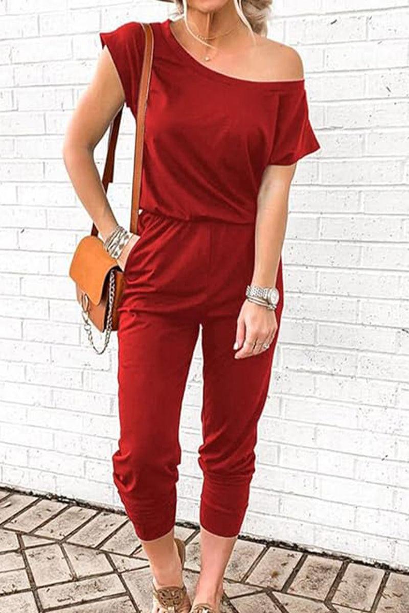 Red Moonlit Rome Off-Shoulder Jumpsuit with elastic waist and tapered legs, styled with tan shoulder bag and silver accessories