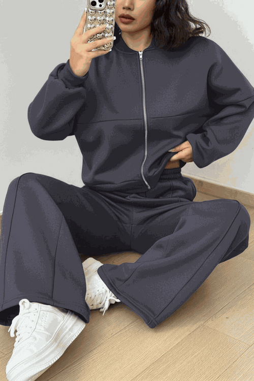 The Voyager Zip Set two-piece zip-front sweatshirt and wide-leg joggers in dark gray with pockets, styled with white sneakers for comfortable travel and casual wear.