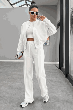 Woman wearing The Voyager Zip Set white zip-front sweatshirt and wide-leg joggers with sneakers in a modern indoor setting