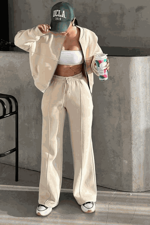 Woman wearing The Voyager Zip Set beige zip-front sweatshirt and wide-leg joggers with pockets, styled casual with sneakers and cap.