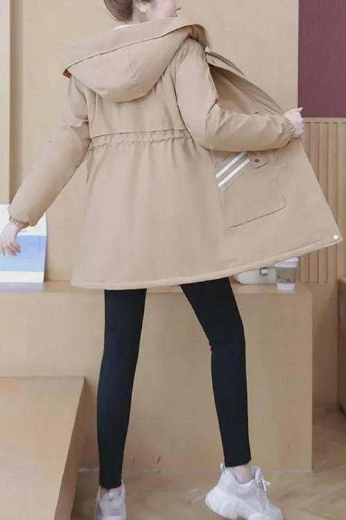 Back view of a woman wearing a beige Cityscape Comfort Hooded Windbreaker with a plush interior and mid-length fit paired with black leggings and white sneakers.