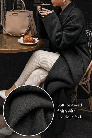 Black oversized teddy coat with soft textured fabric and relaxed fit worn by a seated woman at a café table.