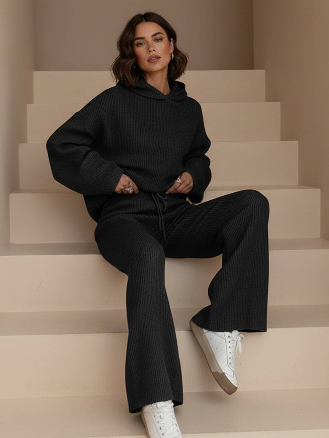 Woman wearing black waffle-knit two-piece hoodie and pants set with white sneakers sitting on beige stairs