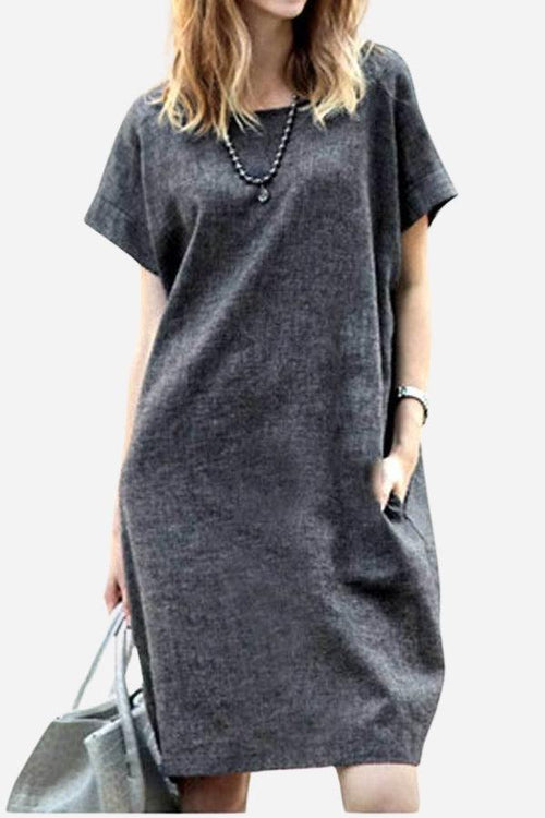 Woman wearing a charcoal gray short sleeve shift dress with side pockets, accessorized with a necklace and gray handbag