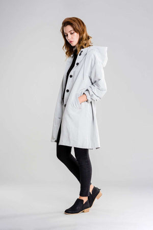 Woman wearing a light gray water-resistant oversized hooded windbreaker rain jacket with black buttons and black leggings.