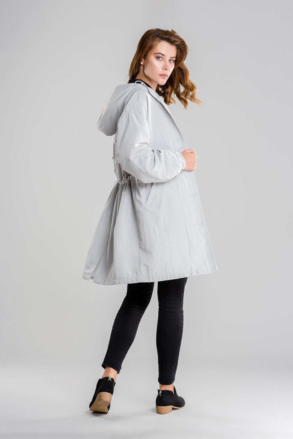 woman wearing light gray oversized water-resistant windbreaker jacket with hood and black pants against gray background