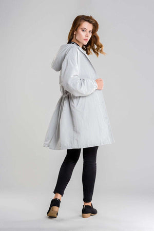woman wearing light gray oversized water-resistant windbreaker jacket with hood and black pants against gray background