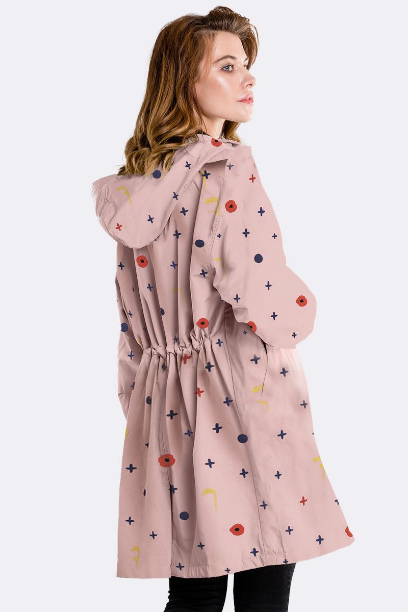 Woman wearing water-resistant oversized windbreaker with hood and colorful pattern on light pink fabric