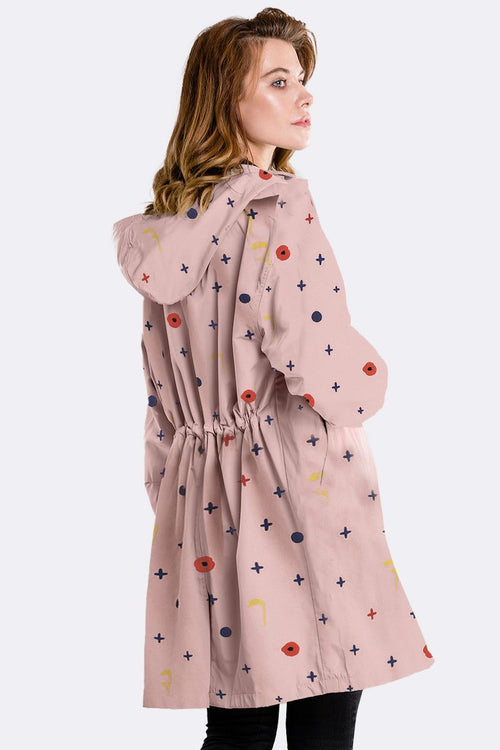 Woman wearing water-resistant oversized windbreaker with hood and colorful pattern on light pink fabric