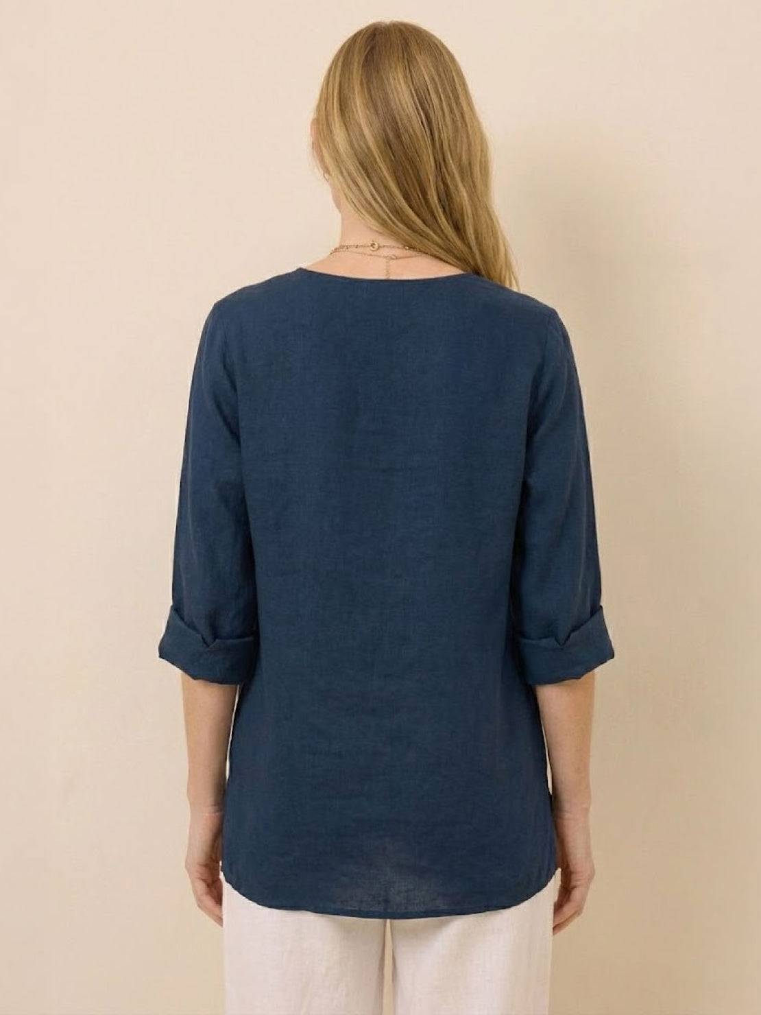 Back view of a woman wearing a navy blue Pure Linen Age-Defying Shirt with rolled-up sleeves and white pants, showcasing breathable and comfortable fabric.
