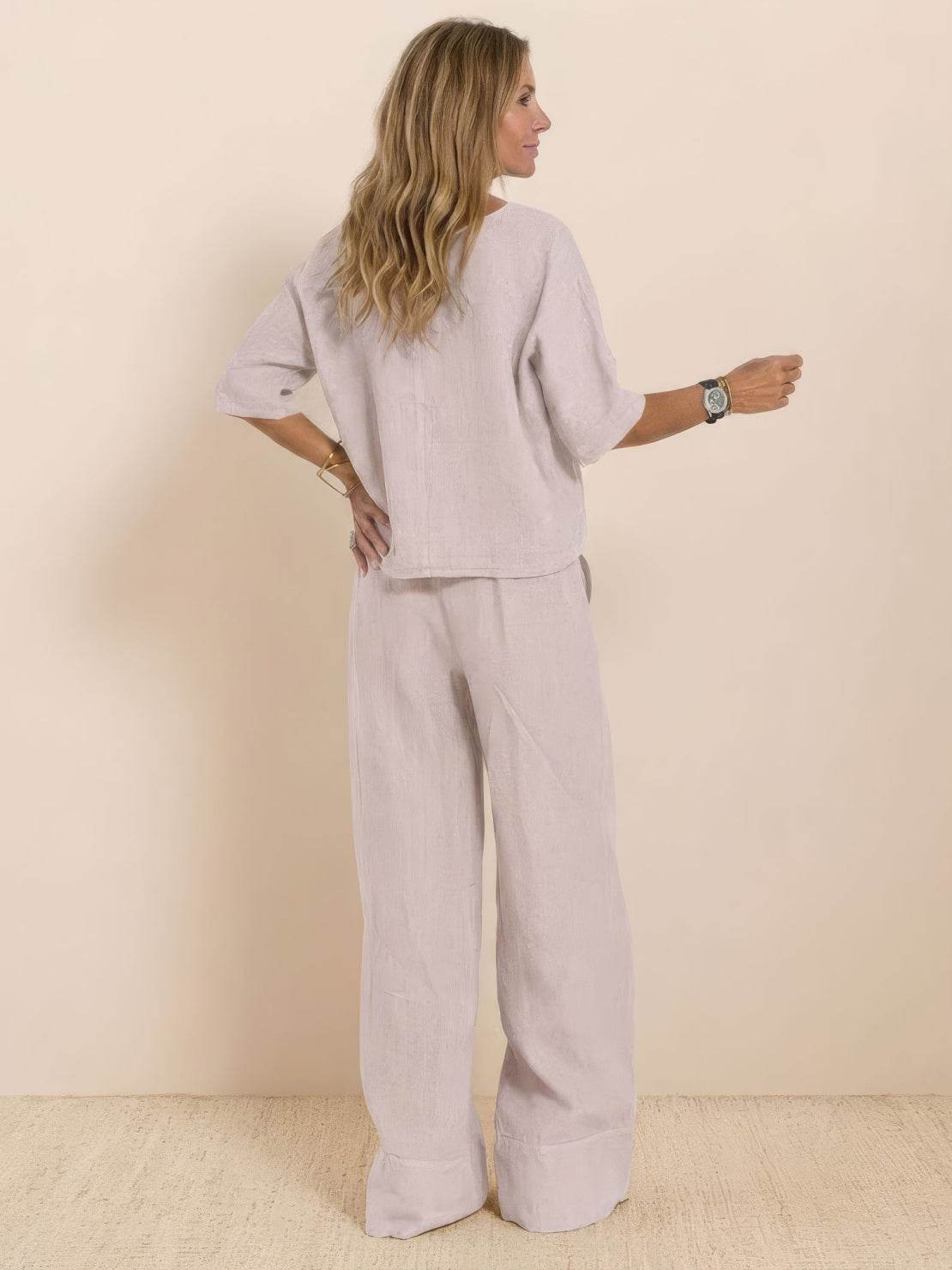 Woman wearing a soft cotton short-sleeved pullover and wide trouser matching set in light beige, viewed from the back.