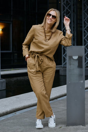 Woman wearing cotton-linen monochrome capsule outfit with longline top and wide-leg pants in tan color, accessorized with sunglasses and necklace outdoors