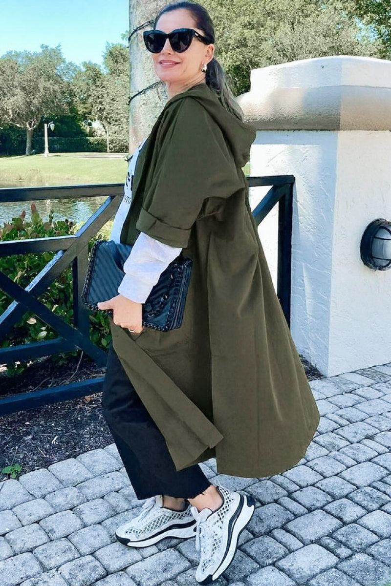 Woman wearing oversized olive green water resistant windbreaker jacket with hood, styled casually outdoors
