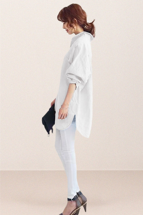 Woman wearing white oversized linen shirt with loose sleeves and flowing hemline, styled with white pants and heels.