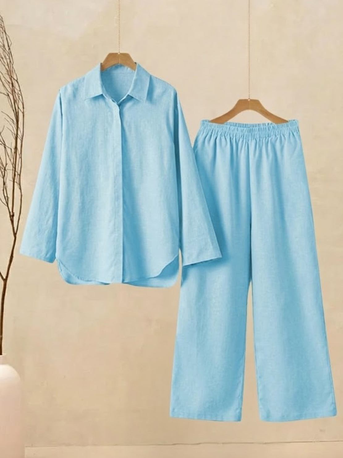 Light blue oversized 100% cotton shirt and wide-leg pants co-ord set hanging on wooden hangers against beige background