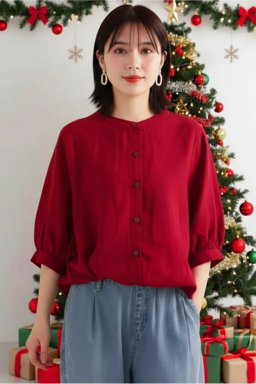Woman wearing a relaxed loose breathable red linen blouse with button-down front in front of a decorated Christmas tree.
