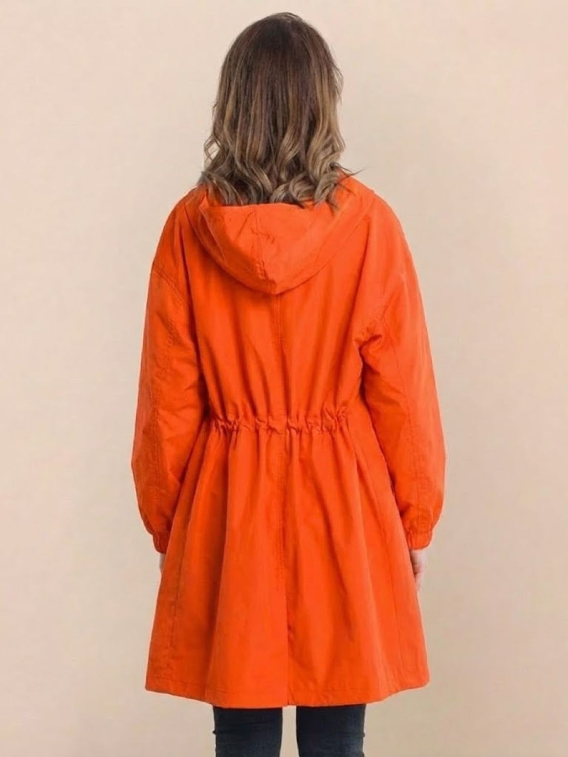 Woman wearing orange Rain Couture Windbreaker oversized water-resistant jacket with hood, back view