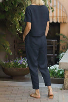 Back view of a woman wearing a relaxed fit black cotton linen set with short sleeves and straight-leg pants.