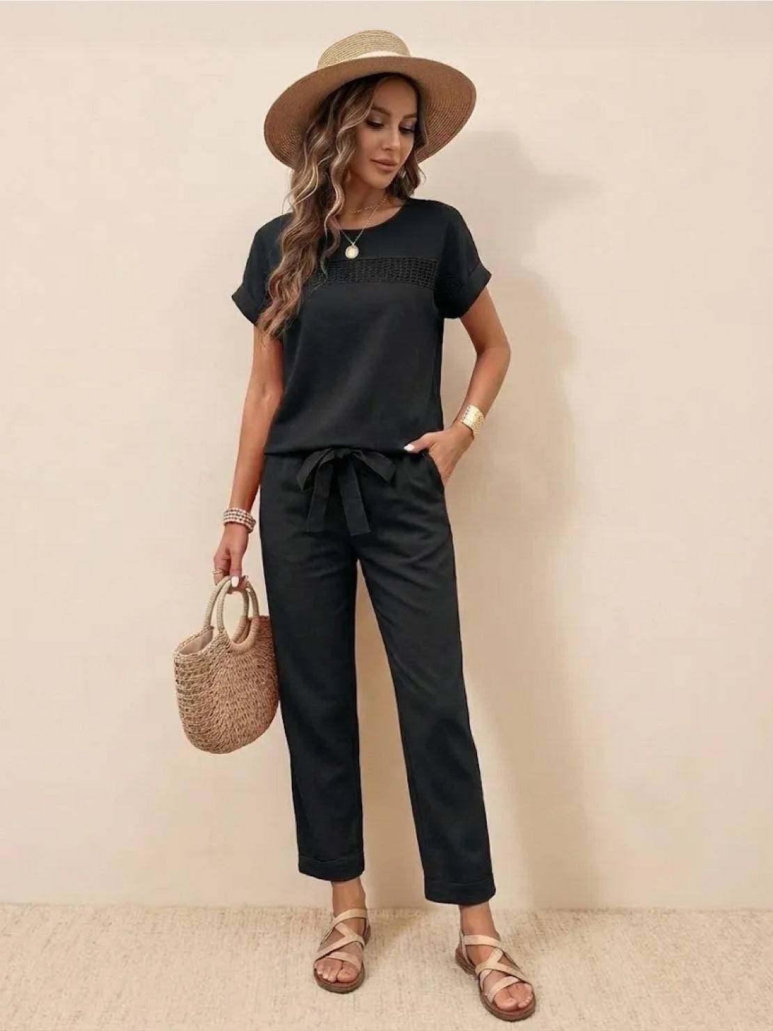 Woman wearing 100% cotton total comfort black two-piece travel set with short sleeves and drawstring pants, accessorized with a straw hat and wicker handbag.