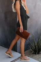 Woman wearing black alluring V-neck layered romper with high waist drawstring and holding brown clutch bag