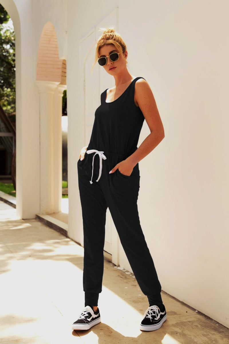 Woman wearing black comfy sleeveless vest pocket jumpsuit with elastic waistband and drawstring outdoors