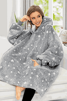 Woman wearing oversized gray Lazy Fleece Blanket Sweater with white stars, sitting indoors and smiling