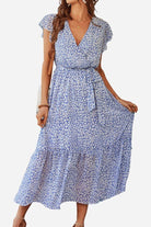 Woman wearing Elegant Blossoms Boho Maxi Dress with floral pattern, V-neck, short sleeves, and belted ruffle hem in soft blue tones.
