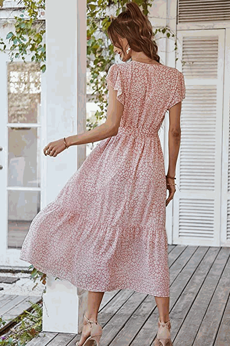 Woman wearing Elegant Blossoms Boho Maxi Dress with floral pattern, short sleeves, and ruffled hem in light pink.